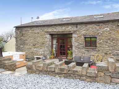 A stone building with an outdoor seating area and hot tub at Hill Side Barn Pennington near Ulverston