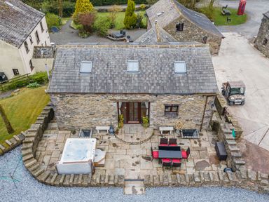 An outdoor stone patio with a hot tub and dining table with chairs outside a stone building at Hill Side Barn in Pennington near Ulverston
