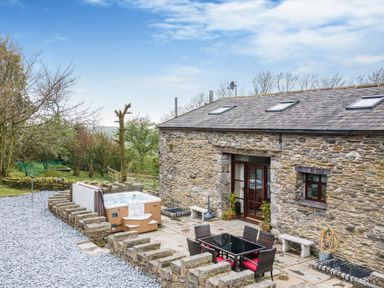 An outdoor patio area with a hot tub black table and chairs beside a stone building at Hill Side Barn Pennington near Ulverston