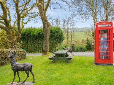 A garden with two deer statues a wooden picnic table and a red telephone box at Hill Side Barn Pennington near Ulverston