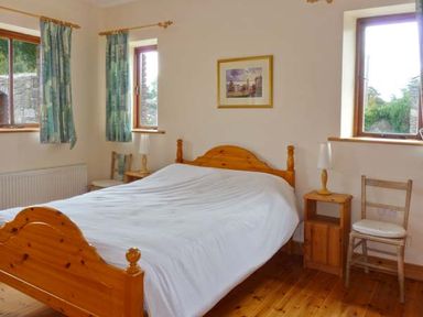 A bedroom with a wooden double bed white bedding two bedside tables with lamps two windows with curtains and wooden chairs at The Range in Enniscorthy County Wexford