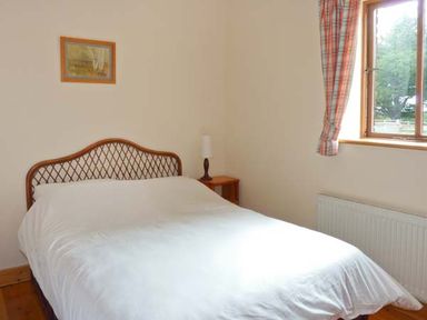 A bedroom with a double bed white bedding a wooden headboard bedside table lamp window with plaid curtains at The Range in Enniscorthy County Wexford