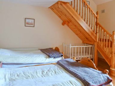 A bedroom with two single beds with blankets a wooden staircase and a white baby crib at The Range in Enniscorthy County Wexford