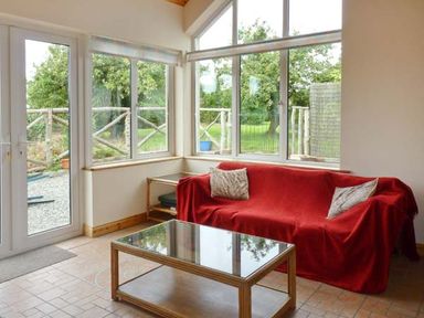 A room with a red covered sofa with two pillows a glass coffee table wooden side table and large windows showing green trees outside at The Range in Enniscorthy County Wexford