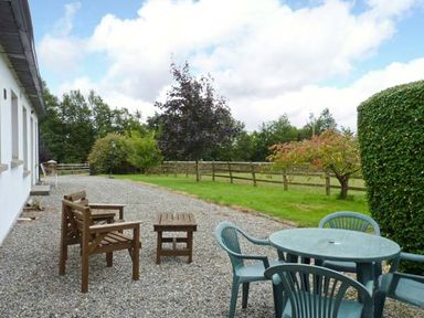 An outdoor patio area with wooden chairs a table and green plastic chairs near a white building at The Range Enniscorthy County Wexford