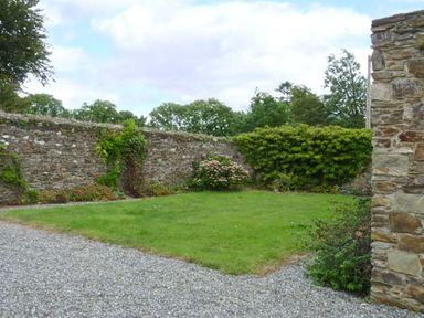 A garden area with grass and a stone wall surrounded by bushes and gravel at The Range in Enniscorthy County Wexford