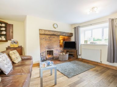 A living room with a leather sofa and coffee table by a fireplace with a TV and window at Ty Nant in Betws-y-Coed