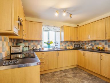 A kitchen with wooden cabinets a toaster a microwave a fruit basket and flowers on the counter at Ty Nant in Betws-y-Coed