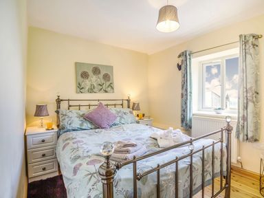 A bedroom with a metal bed frame floral bedding two bedside tables lamps a window with floral curtains and folded towels on the bed at Ty Nant in Betws-y-Coed