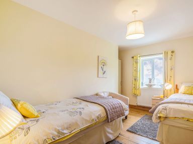 A bedroom with two beds a window with yellow curtains and wooden floor at Ty Nant in Betws-y-Coed