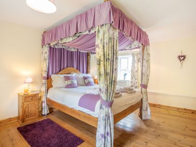 A bedroom with a wooden four-poster bed with purple and floral curtains and bedding at Ty Nant in Betws-y-Coed