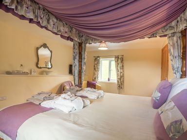 A bedroom with a canopy bed purple pillows and a window with floral curtains at Ty Nant in Betws-y-Coed