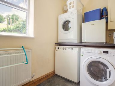 A utility room with a washing machine dryer dryer and laundry basket on a worktop at Ty Nant in Betws-y-Coed