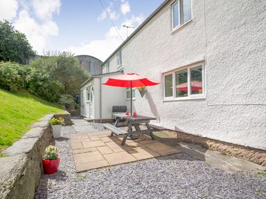 A patio area with a wooden picnic table and red umbrella next to a white house with stone and gravel ground at Ty Nant in Betws-y-Coed