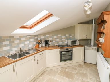A kitchen with a skylight, stove, oven, microwave, sink, wooden countertops, and cabinets at Foxglove Cottage in Little Haven near Haverfordwest