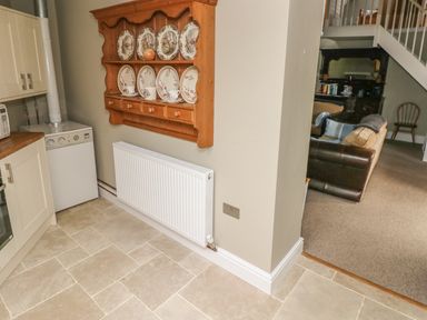 A kitchen area with a wooden plate rack and a white radiator next to a living room with a brown leather sofa and staircase at Foxglove Cottage in Little Haven near Haverfordwest