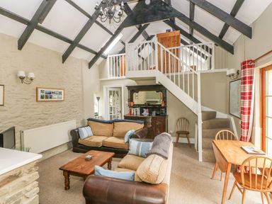 A living room with sofas a wooden coffee table a staircase leading to a loft and a dining table with chairs at Foxglove Cottage in Little Haven near Haverfordwest