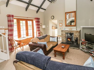 A living room with a stone fireplace wood stove sofas wooden coffee table and a dining table by glass doors at Foxglove Cottage in Little Haven near Haverfordwest