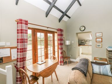A dining area with a table and chairs next to glass doors with red plaid curtains in a room with exposed ceiling beams at Foxglove Cottage in Little Haven near Haverfordwest