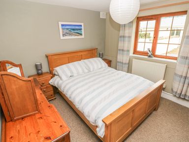 A bedroom with a wooden double bed a dresser with mirror two bedside tables lamps a window and a painting at Foxglove Cottage in Little Haven near Haverfordwest
