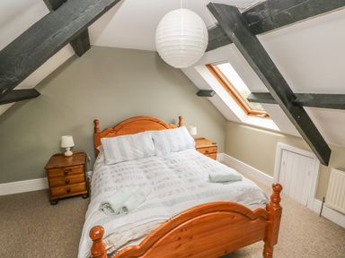 A bedroom with a wooden bed frame, two bedside tables with lamps, a skylight window, and exposed ceiling beams at Foxglove Cottage in Little Haven near Haverfordwest