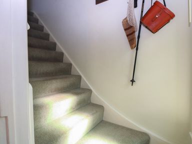 Carpeted staircase with bags and a walking stick hanging on a white wall at Peggotty's in Kelsale near Saxmundham
