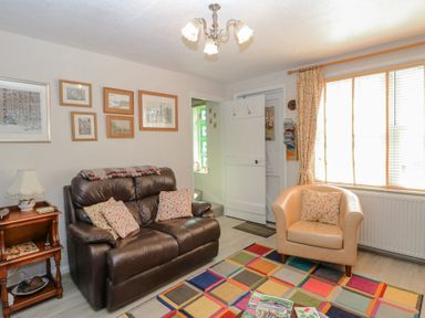 A living room with a brown leather sofa and a beige armchair near a window with curtains at Peggotty's in Kelsale near Saxmundham