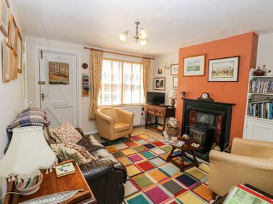 A living room with a leather sofa, armchairs, a fireplace, a wooden table, and a multicolored square patterned rug at Peggotty's in Kelsale near Saxmundham