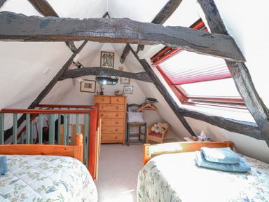 A bedroom with wooden beds and exposed wooden beams a chest of drawers and a window with a red blind at Peggotty's in Kelsale near Saxmundham