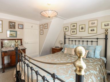 A bedroom with a metal bed frame a wooden side table with a lamp and a wooden dresser with towels and framed pictures on the wall at Peggotty's in Kelsale near Saxmundham