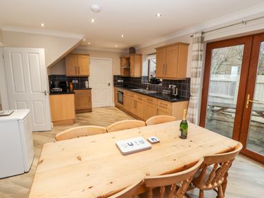 A kitchen with wooden cabinets a wooden dining table with chairs and glass doors leading outside at Bryn Seion in Y Felinheli