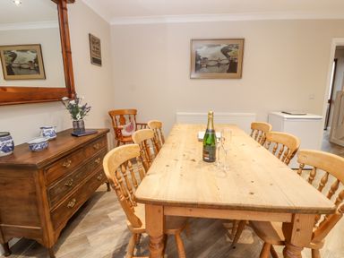 A dining room with a wooden table and six chairs a wooden dresser with ceramic items flowers and a large mirror at Bryn Seion in Y Felinheli