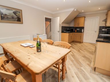 A kitchen and dining area with a wooden table and chairs a bottle and glasses on the table wooden cabinets and a framed picture on the wall at Bryn Seion in Y Felinheli