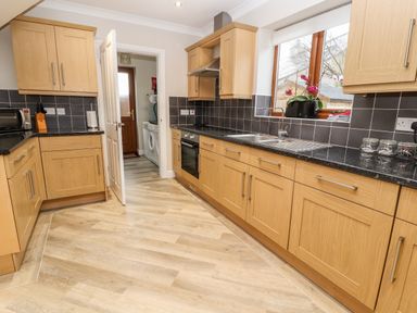 A kitchen with wooden cabinets black countertops a stainless steel sink and a door leading to a utility room at Bryn Seion in Y Felinheli