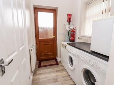 A utility room with washing machines a fire extinguisher an ironing board and a wooden door at Bryn Seion in Y Felinheli