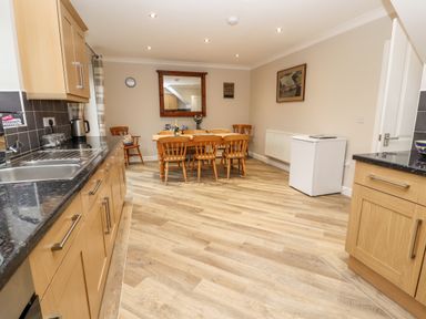 A kitchen with wooden cabinets a dining table with six chairs and a small white refrigerator in Bryn Seion Y Felinheli