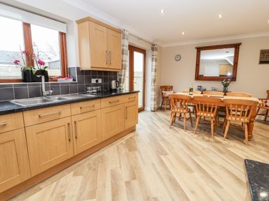 A kitchen and dining area with wooden cabinets a black countertop a dining table with wooden chairs a large mirror and a window at Bryn Seion in Y Felinheli