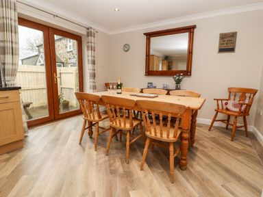 A dining area with a wooden table and six chairs near glass doors in a room at Bryn Seion in Y Felinheli