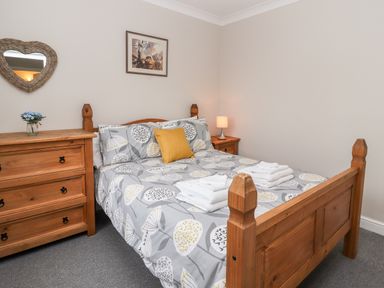 A bedroom with a wooden bed and bedside tables with lamps and a chest of drawers with a heart shaped mirror on the wall at Bryn Seion in Y Felinheli