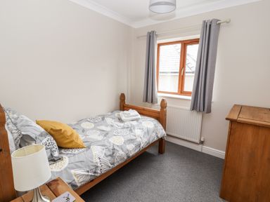 A bedroom with a single bed next to a window a wooden chest of drawers and a bedside table with a lamp at Bryn Seion in Y Felinheli