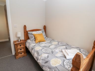 A bedroom with a single wooden bed with floral bedding a yellow cushion a wooden bedside table and a lamp at Bryn Seion in Y Felinheli