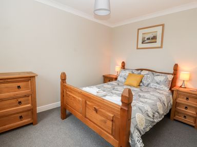 A bedroom with a wooden bed and matching bedside tables with lamps at Bryn Seion in Y Felinheli