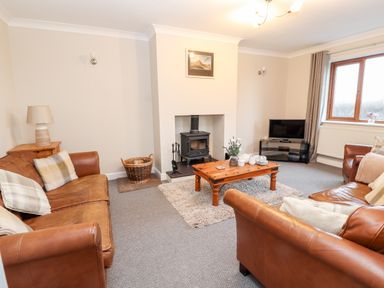 A living room with leather sofas wooden coffee table wood stove and television at Bryn Seion in Y Felinheli