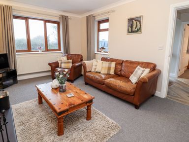 A living room with brown leather sofa and armchair wooden coffee table with vase and teapot at Bryn Seion in Y Felinheli