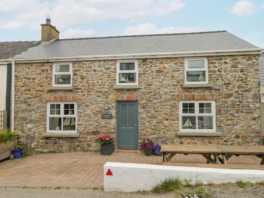 Stone house with blue door and windows with flower pots and wooden bench at Hillbrook House in Nolton Haven
