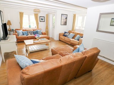 A living room with three brown leather sofas a wooden coffee table and a television at Hillbrook House in Nolton Haven