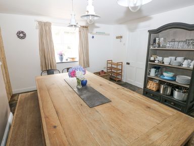 A dining room with a wooden table and flower vase and a cabinet with dishes and pots at Hillbrook House in Nolton Haven