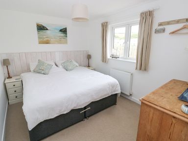 A bedroom with a double bed two side tables two lamps a window with curtains a wooden dresser and a painting above the bed at Hillbrook House in Nolton Haven