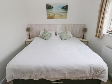 A bedroom with a double bed white bedding two pillows with boat print bedside tables and lamps and a beach painting above the bed at Hillbrook House in Nolton Haven