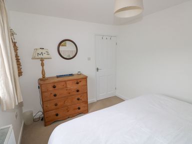 A bedroom with a wooden dresser with a lamp and a round mirror above it at Hillbrook House in Nolton Haven
